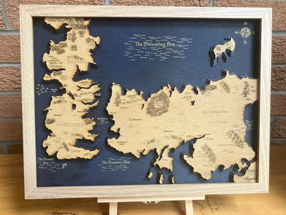 Framed 3D wooden relief map of Westeros and Essos with engraved seas, regions and a compass on a deep blue background