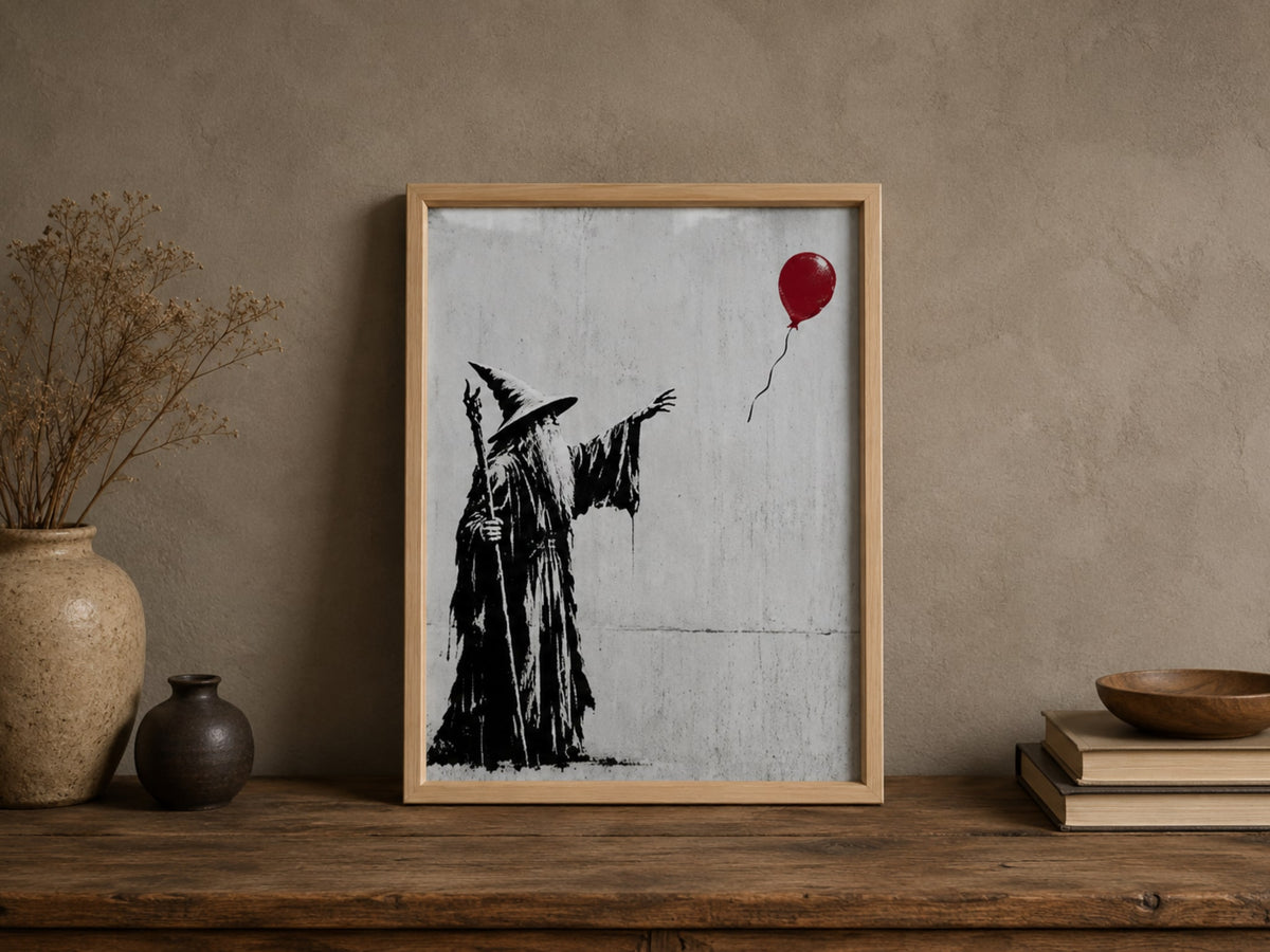 Oak framed street art print of a wizard with a staff reaching for a red balloon, on a shelf beside a vase and books