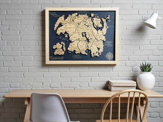 Framed 3D wooden relief map of Tamriel on a navy background, hanging on a white brick wall above a desk