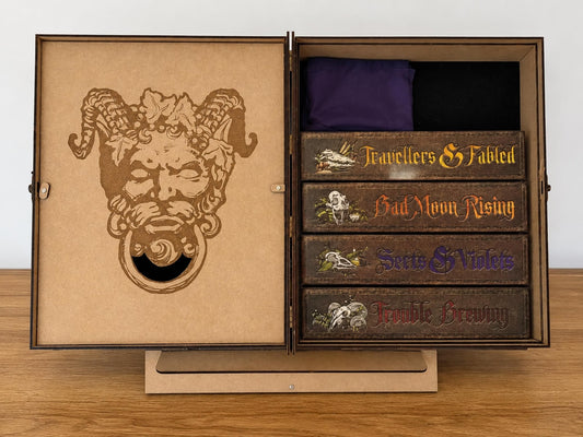 Open wooden grimoire engraved with a horned demon face, holding coloured token trays on a fold-out stand