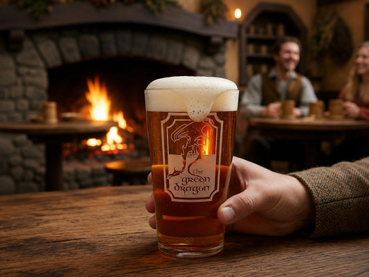 Hand holding a pint of beer engraved with the Green Dragon pub sign, in a busy tavern with a fire behind