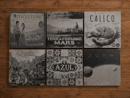 Six square slate coasters engraved with board game box art including Calico, Azul, Dune and Terraforming Mars