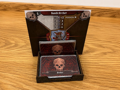 Dark wooden deck holder with a Bandit Archer stat card standing behind and a skull-backed monster ability deck in front