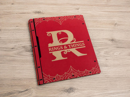 Red wooden book box with a gold engraved R monogram and the words Rings & Things, with web corner patterns, on a light table