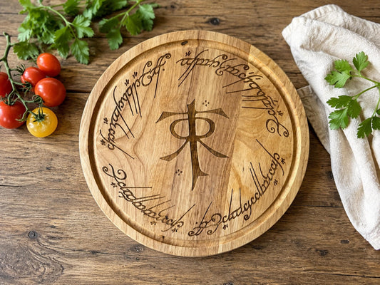 Round wooden chopping board engraved with the Tolkien monogram ringed by Elvish-style script, with tomatoes