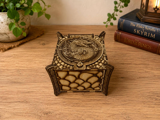 Small wooden box engraved with dragon scales and a coiled dragon on the round lid, beside fantasy books