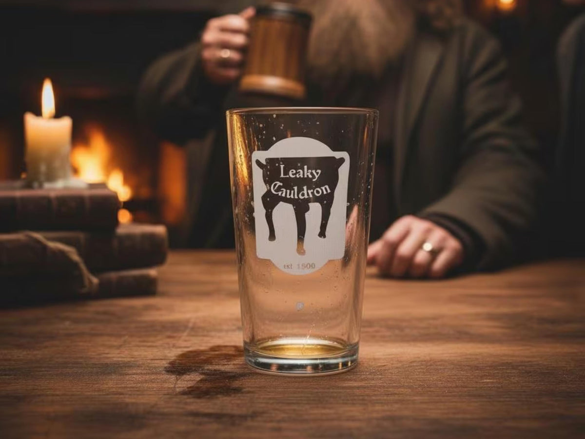 Empty pint glass engraved with the Leaky Cauldron pub sign on a wooden table by candlelight