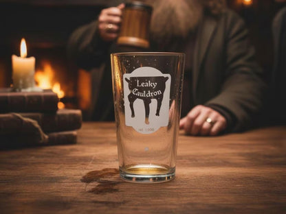 Empty pint glass engraved with the Leaky Cauldron pub sign on a wooden table by candlelight