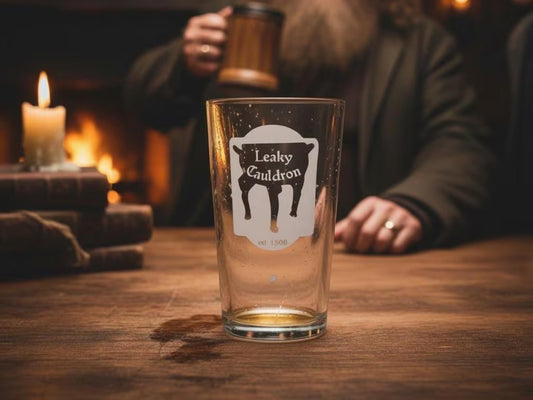 Empty pint glass engraved with the Leaky Cauldron pub sign on a wooden table by candlelight