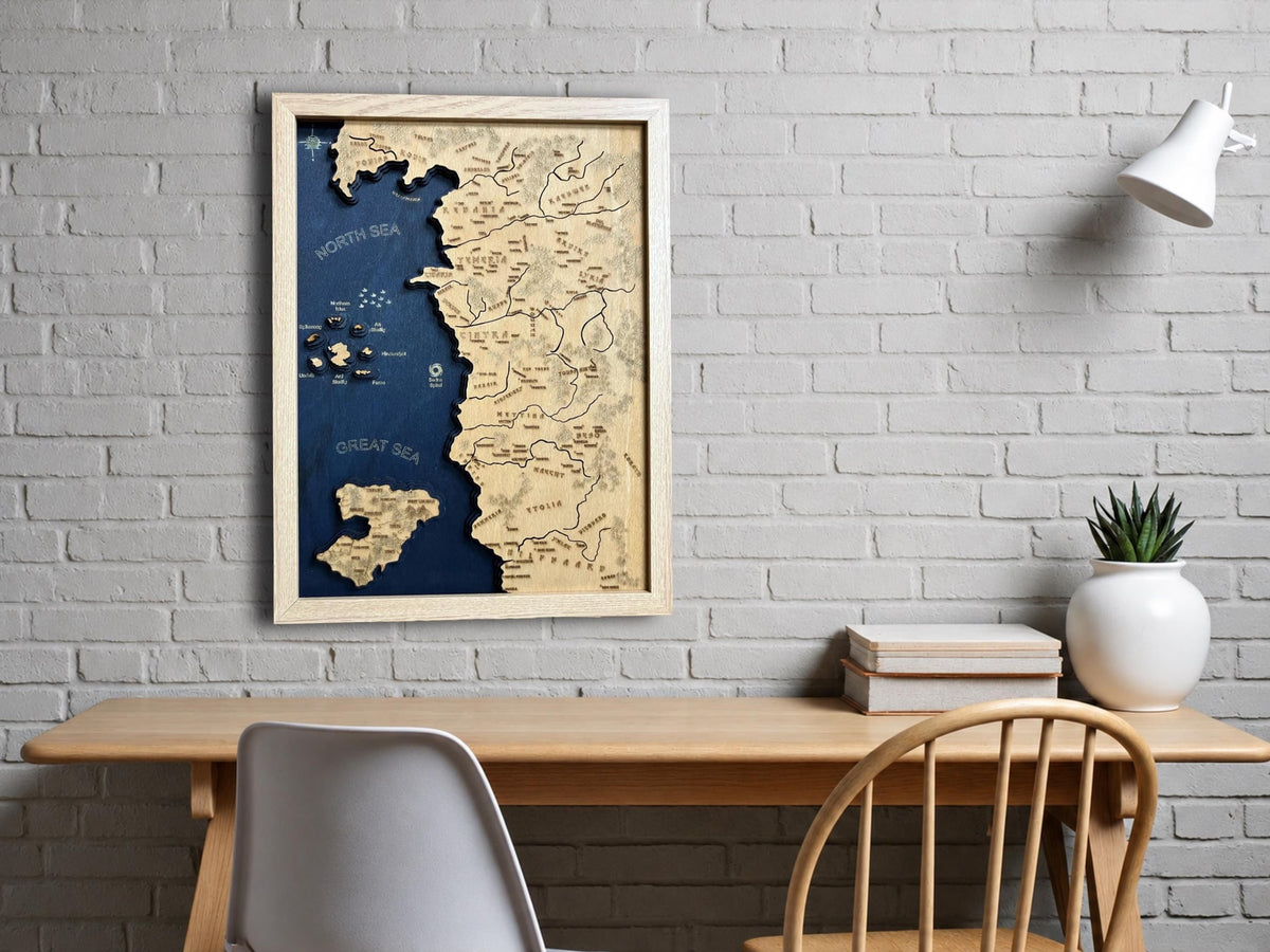 Framed wooden 3D relief map of The Witcher world on a navy sea, hanging above a desk on a white brick wall