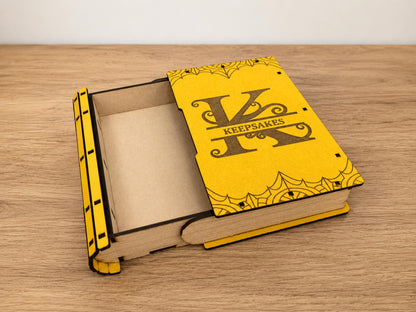 Yellow book-shaped box with a sliding lid open, the cover engraved with a large K monogram and Keepsakes