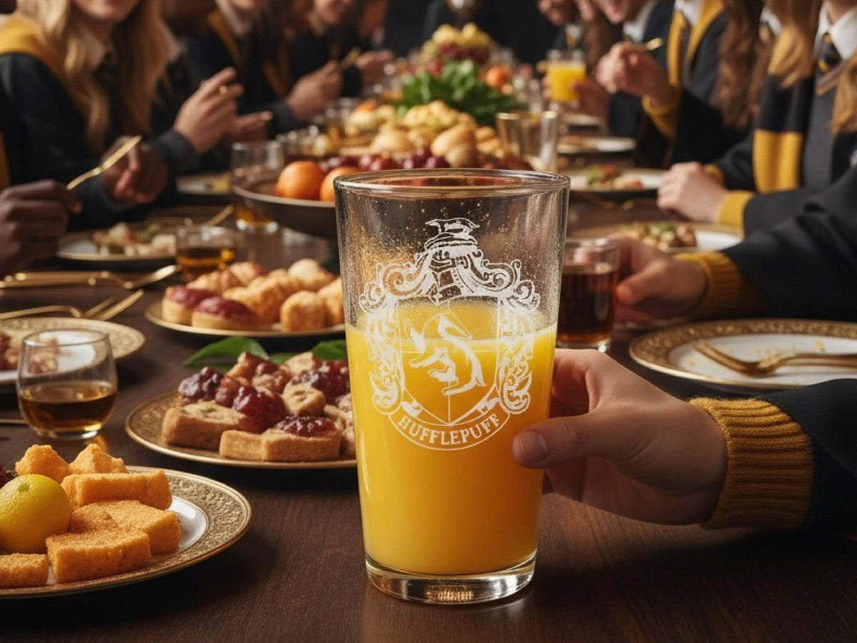 Pint glass engraved with the Hufflepuff house shield, filled with orange juice at a feast table