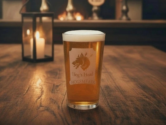 Pint glass of beer engraved with the Hog's Head Hogsmeade pub sign, beside a candle lantern
